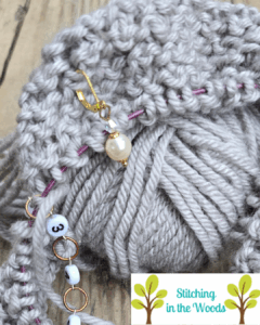 A grey ball of yarn sits behind a knitting project in progress, visible is the row counter, a stitch marker, and the circular cable needle