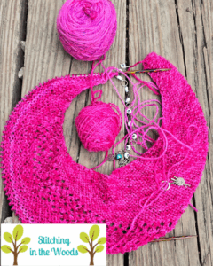 Pink shawl in progress lays on a wooden deck