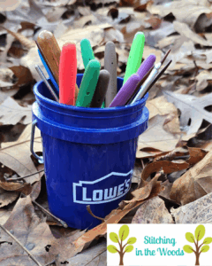 A mini version of a Lowe's 5 gallon bucket sits on some leaves.  Sticking out of it are the handles of hooks and some DPNs.