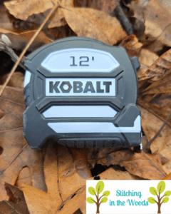 a black and white 12 foot Kobalt tape measure lying on some leaves; Kobalt is a Lowe's brand